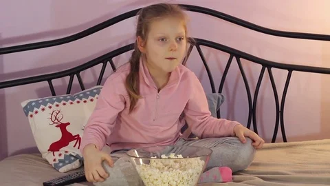 Happy young girl is eating popcorn and watching TV at home Stock Footage
