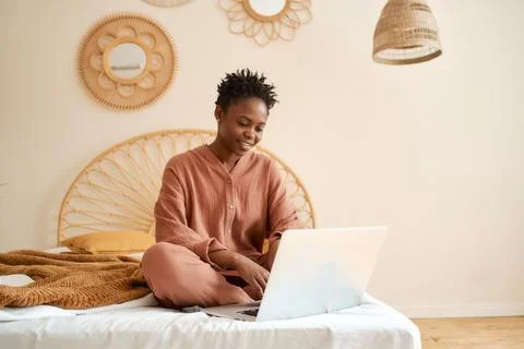 Happy Young girl sitting on bed in bedroom and using laptop. Muslin pajama Stock Photos