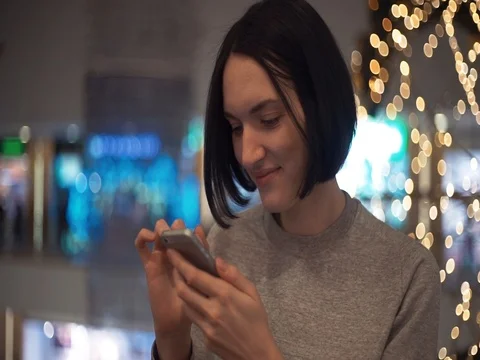 Happy young girl smiling using smartphone chatting online in shopping mall Stock Footage 83368902