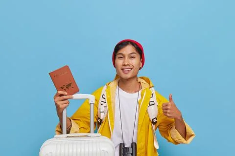 Happy young guy in jacket showing thumb up and his passport ready to go for trip Stock Photos