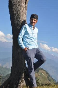 A happy young guy looking at camera while posing with leaning against tree Stock Photos