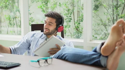 Happy young handsome freelancer man resting with feet on desk while sitting o Stock Footage 134399243