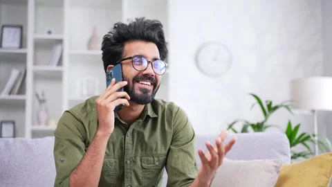 Happy young handsome man talking on smartphone while sitting on sofa in living  Stock Footage 252200643