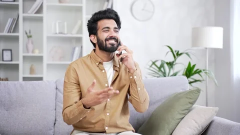 Happy young handsome man talking on smartphone while sitting on sofa in living  Stock Footage 252205539