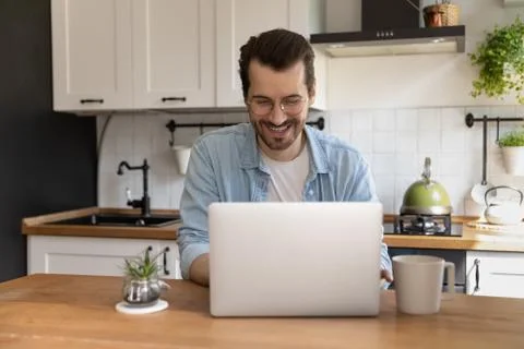 Happy young handsome man using computer in kitchen. Foto stock