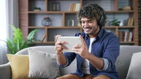 Happy young handsome man in wireless headphones plays a video game on a digital  Stock Footage 297871811
