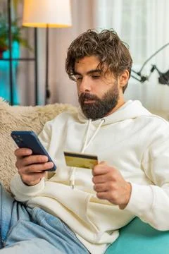 Happy young Hispanic man guy using credit bank card and cellphone while shopping Stock Photos