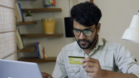 Happy young Indian man using laptop at home and holding credit card. Video stock 155577003