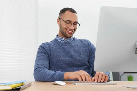 Happy young intern working with computer at table in modern office Stock Photos