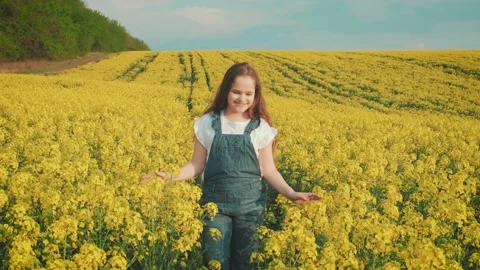Happy young joyful cute smiling girl walks spring blooming yellow rape field Stock Footage 134574892