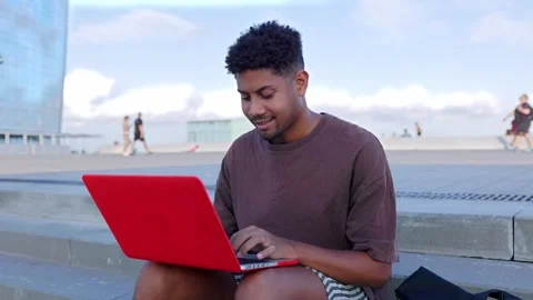 Happy young latin man using laptop computer sitting outdoors Stock Footage 250837964