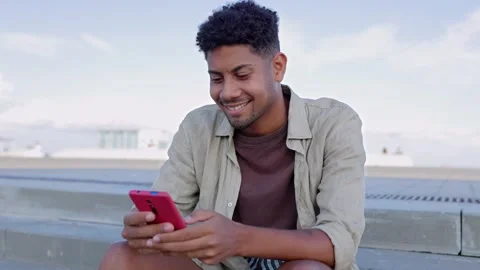 Happy young latin man using cell phone sitting outdoors Stock Footage 250838079