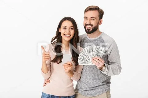 Happy young loving couple holding money showing thumbs up using mobile phone. Stock-Fotos