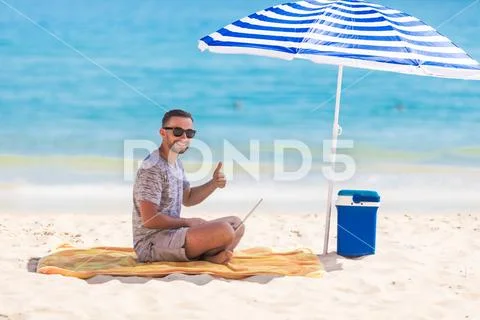 Happy young man in the beach under umbrella near the ocean working on his lap Stock Photos