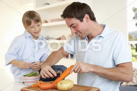 Happy young man with boy peeling vegetables in kitchen Stock Photos