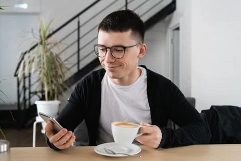 Happy young man browsing internet on smartphone sitting at outdoor cafe. Foto stock