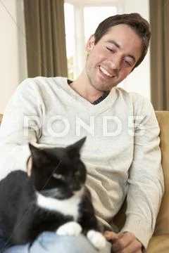 Happy young man with cat sitting on sofa Stock Photos