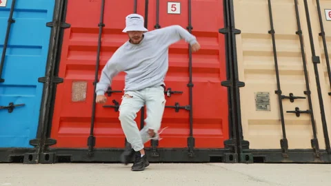 Happy young man dancer moves to music smiling of red color containers summer Stock Footage 155073530
