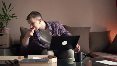 Happy young man eats pizza and works at the computer. home interior. Stock Footage 207782045