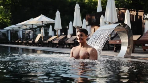 Happy young man enjoying spa pool waterfall jet massage at resort on vacation Stock Footage 333564910