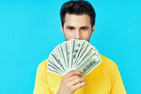 Happy young man holding stack of money and boasting his savings on blue Stock-Fotos