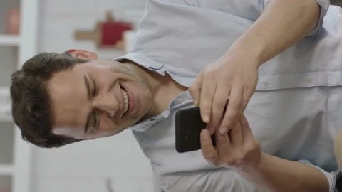 Happy young man looking at mobile phone at home Stock Footage 196116602
