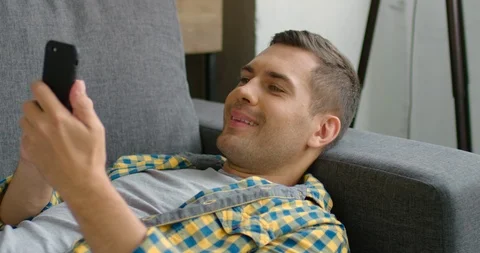 Happy young man lying on couch, using his smartphone Stock Footage 113615130