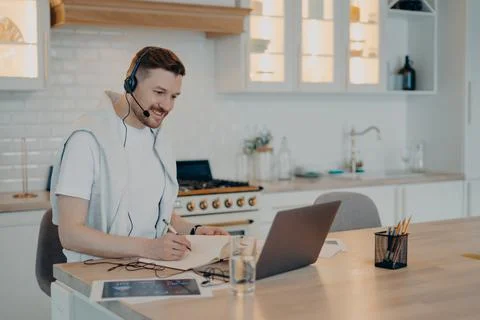 Happy young man making notes in notebook during a video call Stock Photos