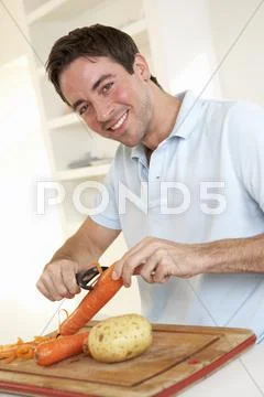 Happy young man peeling vegetable in kitchen Stock Photos