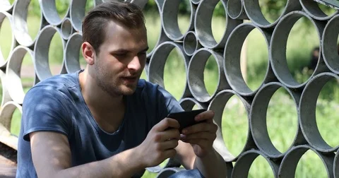 Happy Young Man Playing Game on Smartphone in Park Celebrating Winning Stage Day Stock Footage 70660194