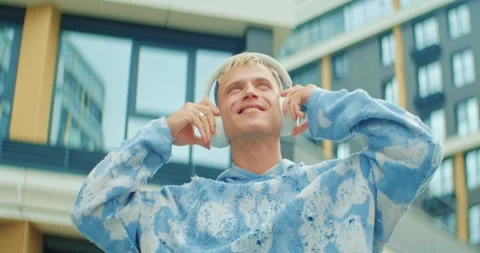 Happy young man puts on wireless headphones and enjoys music in the city 動画素材 303597683