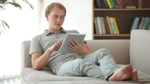 Happy young man relaxing on couch using touchpad looking at camera and smiling Stock Footage 34279560
