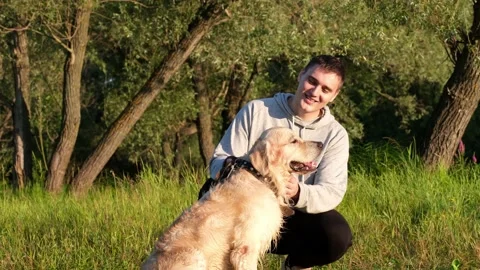Happy young man scratching his dog at dawn on the green grass. Stock Footage 202315518