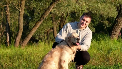 A happy young man scratching his dog at dawn on  green grass. Stock Footage 202315524