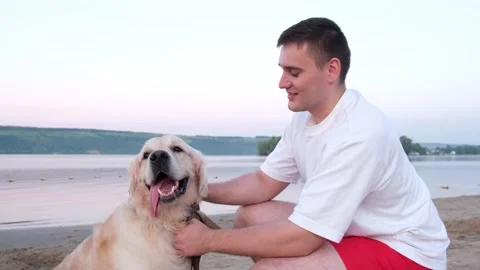 A happy young man scratching his dog at dawn on the riverbank. Stock Footage 202315542