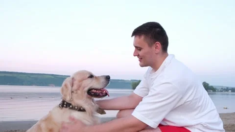 A happy young man scratching his dog at dawn on the riverbank. Stock Footage 202315549