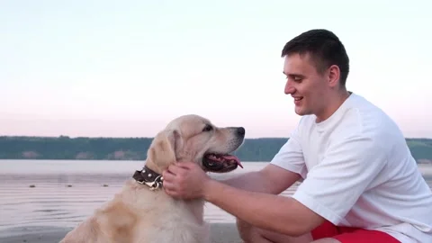 A happy young man scratching his dog at dawn on the riverbank. Stock Footage 203828724