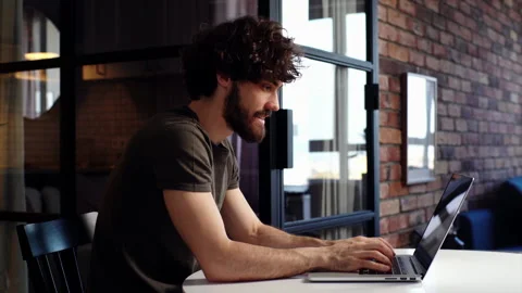 Happy young man sits down at desk, opening laptop and starts typing on keyboard Video stock 149986905