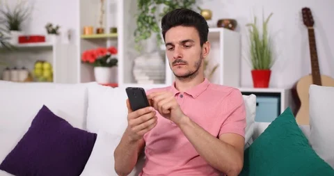 Happy Young Man Sitting on Sofa Using Mobile Phone to Looking at Friends Photos Stock Footage 87912352