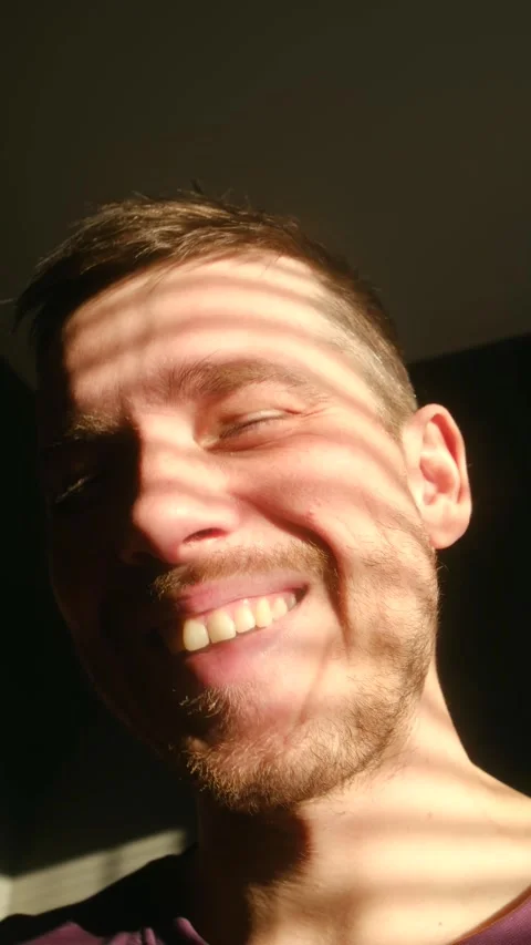 Happy young man smiling with sunlight through blinds on his face Stock Footage 323207941