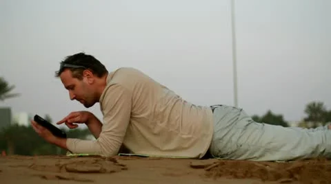 Happy young man with tablet computer lying on the beach Видео 10763948