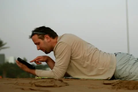 Happy young man with tablet computer lying on the beach Stockbeeldmateriaal 10791859