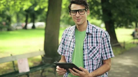 Happy young man with tablet computer in park, steadicam shot HD Video stock 11824784