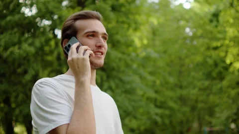 Happy young man talking on a mobile phone in a green park. Phone call. Stock Footage 335206713