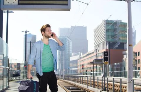 Happy young man talking on mobile phone at train station platform Stock Photos