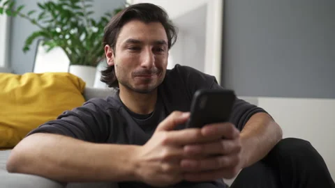 Happy young man texting message on mobile phone while staying at home Stock Footage 149255598