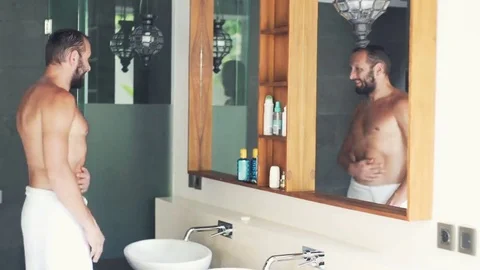 Happy, young man in towel checking his body in mirror in bathroom Stock Footage 69147942