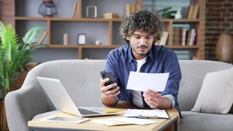 Happy young man uses mobile app for spending bills using smartphone while sit Stock Footage 297873247