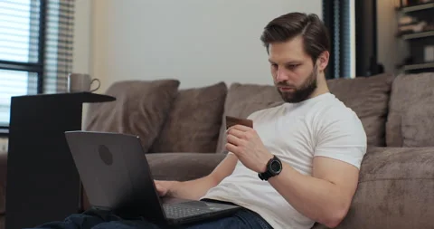 Happy young man using credit card and laptop computer in living room, online Stock Footage 269143574