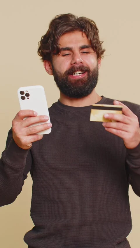 Happy young man using credit card and smartphone while transferring money Stock Footage 323365316